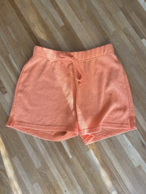 Orange stickade shorts med snörning - Snygga orange stickade shorts med snörning i midjan. De har en avslappnad passform och är perfekta för varma dagar. Materialet känns mjukt och bekvämt mot huden.