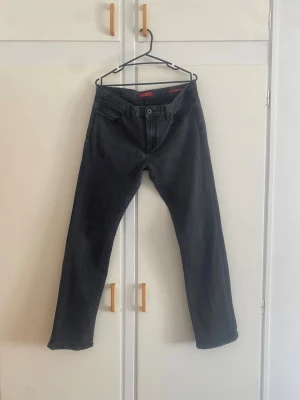 Guess svarta jeans - Säljer ett par svarta jeans med rak passform och klassisk femficksdesign. Jeansen har knappgylf och bälteshällor. Materialet är denim i bomull och färgen är tvättad svart, vilket ger en cool och avslappnad look.