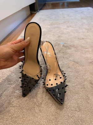 Svarta pumps med nitar från Public Desire - Säljer ett par svarta pumps från Public Desire med transparent plast och spetsig tå. Skorna har höga klackar och är dekorerade med svarta nitar över hela ovandelen. Snygg och edgy design som sticker ut.