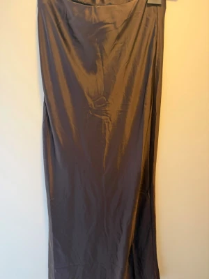Brun långkjol i satin från Bik Bok - Snygg brun långkjol i satin från Bik Bok. Kjolen har en slät och glansig yta som ger en lyxig känsla och faller fint längs kroppen. Perfekt att styla med en enkel topp eller stickad tröja för en trendig look.