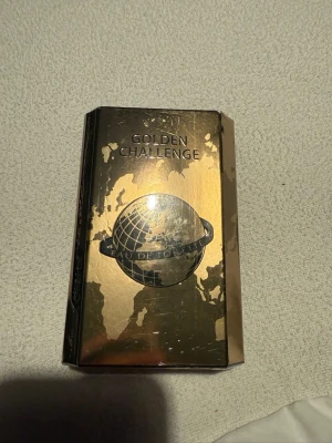 Golden Challenge Eau de Toilette - Golden Challenge Eau de Toilette från Omerta kommer i en lyxig, guldglänsande rektangulär förpackning med världskarta och globmotiv. Flaskan har en modern och exklusiv look, perfekt för dig som gillar stilrena och iögonfallande parfymer.