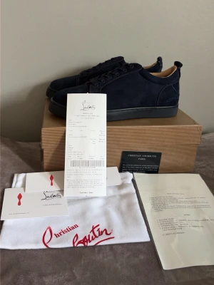 Marinblå sneakers från Christian Louboutin - Snygga marinblå sneakers från Christian Louboutin i mocka med klassisk röd sula. Lågt skaft och ton-i-ton snörning ger en clean look. Kommer med originalkartong, dustbag och äkthetskort. Perfekta för dig som gillar exklusiva detaljer och grisch stilen! Allt og medkommer så hör av er vid minsta fundering! Mvh Quadra Closet!
