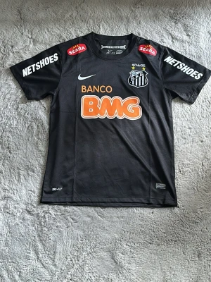 Svart Santos Neymar Jr matchtröja - Säljer en svart Santos FC matchtröja från Nike med Neymar Jr och nummer 11 på ryggen. Tröjan har tryckta sponsorer som BMG, Netshoes och Seara samt klubbmärke på bröstet. Tillverkad i lätt och ventilerande material, perfekt för fotboll eller streetwear.