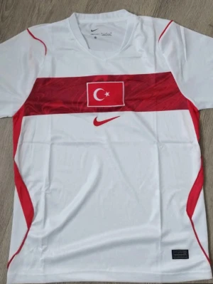 Turkiet Nike matchtröja röd/vit - Snygg vit matchtröja från Nike med Turkiets flagga och röd Nike-logga på bröstet. Tröjan har röda detaljer längs sidorna och ett stort rött fält över bröstet. Tillverkad i lätt och ventilerande material, perfekt för fotboll eller träning.