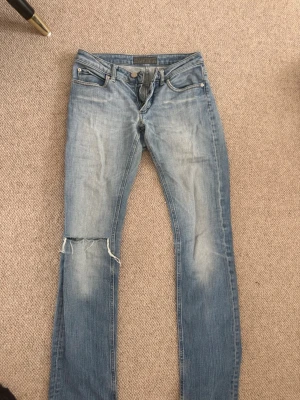 Ljusblå slitna jeans med hål - Säljer ett par ljusblå jeans med slitningar och hål på ena knät. Jeansen har raka ben och slitna detaljer på bakfickorna. Köpte dom på plick men och de är i mycket bra skick 