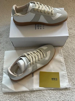 Vita och beige sneakers Maison Margiela - Maison Margiela sneakers – Vita – Storlek 43  Säljer ett par exklusiva vita Maison Margiela sneakers i storlek 43. Skorna är helt nya, oanvända och i perfekt skick. En stilren modell med hög komfort och premiumkänsla som passar både till vardags och mer uppklädda outfits.  * Färg: Vit * Storlek:  * Skick: Helt nya * Levereras med originalkartong om så önskas.  Hör gärna av dig om du vill veta mer eller få fler bilder.