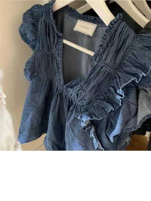 Neo noir blus  - Supersöt blå blus med volangdetaljer och v-ringning. Blusen är ärmlös och har en lös passform, perfekt för varmare dagar. Tillverkad i bomull för en skön känsla. Enkel att styla med både jeans och kjol. Helt oanvänd 