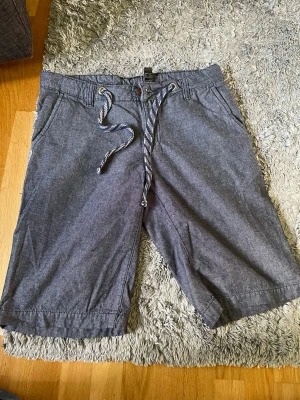 Blåa  shorts med snörning från Livergy - Säljer ett par blåa shorts från Livergy med snörning i midjan och två sidofickor. De har en avslappnad passform och är perfekta för varma dagar. Materialet känns mjukt och bekvämt, och färgen är lätt att matcha med olika plagg.