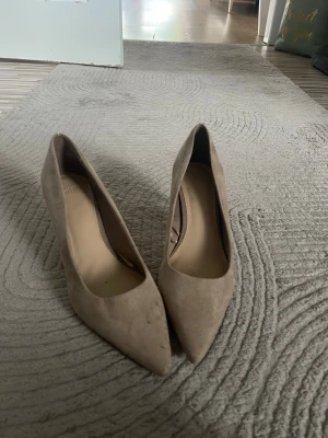 Beige mocka-pumps med spetsig tå - Snygga pumps från H&M i beige mockaimitation med spetsig tå och klassisk siluett. Skorna har en stilren design och passar perfekt till både jeans och klänning. Klacken är medelhög och materialet ger en lyxig känsla.