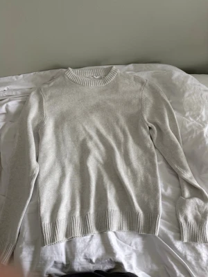 Ljusgrå stickad tröja Dobber - Ljusbeige stickad tröja från Dobber i storlek L. Tröjan har rund halsringning, ribbade muddar vid ärmslut och nederkant samt en enkel, klassisk design. Perfekt för lager på lager och passar till det mesta.