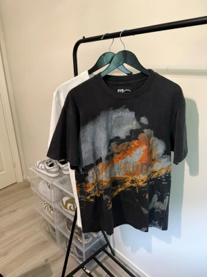 Godspeed T-shirt - Cool svart oversized t-shirt med färgstarkt tryck framtill i orange och grått samt textdetaljer. Baksidan har ett stort paisleymönster och text i vitt. T-shirten har rund hals och korta ärmar, perfekt för en streetwear-look.
