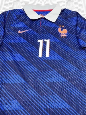 Blå Frankrike matchtröja Olise #11 - Säljer en blå matchtröja från Nike för Frankrikes landslag med Olise och nummer 11 på ryggen. Tröjan har ett mönster i olika blå nyanser, vita detaljer och officiella tryck på ärmarna. Tillverkad i lätt och ventilerande material, perfekt för fotboll.