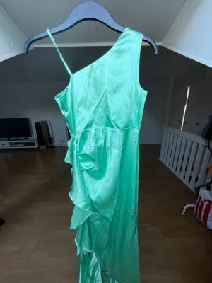 Mintgrön klänning - Säljer en mintgrön klänning i glansigt material och har volangdetaljer längs sidan💚klänningen är helt oanvänd!!