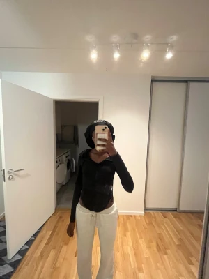 Svart hoodie med dragkedja - Säljer en svart hoodie med dragkedja framtill och huva med snören. Modellen är figurnära och har långa ärmar och öppet vid båda sidorna av höfterna. Perfekt för en chill och avslappnad stil. Materialet känns mjukt och stretchigt, vilket gör den bekväm att bära hela dagen.