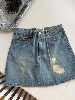 Jeanskjol från Zadig & Voltaire - Trendig jeanskjol i blå denim från Zadig & Voltaire. Kjolen har lagade slitningar framtill, klassiska fickor. Perfekt för dig som gillar en cool och avslappnad stil. Kostar 175€ och aldrig använt. 