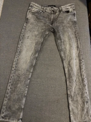 Grå tvättade slim jeans - Säljer ett par grå tvättade jeans med slim passform. Jeansen har klassisk femficksdesign, knappgylf och bälteshällor. Snyggt slitna detaljer och en cool tvättad look som passar till det mesta.