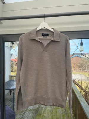 Beige merinoullströja från Riley - Snygg beige långärmad tröja från Riley i mjuk merinoull. Tröjan har klassisk krage och avslappnad passform, perfekt för en stilren look. Ribbstickade muddar vid ärmslut och nederkant ger en clean finish. Nypris är 899