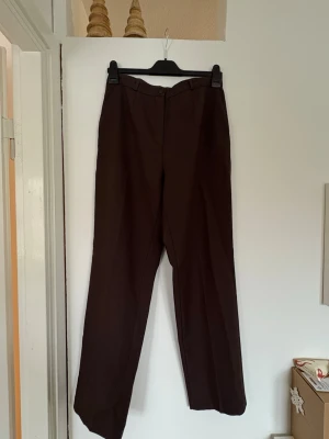 Mörkbruna kostymbyxor  - Ett par högmidjade, mörkbruna kostymbyxor i storlek M. Köpta secondhand och därav vet jag inte märket. Mycket gott skick och bra kvalitet i tyget. Endast använda en gång av mig (säljs då de är fel storlek för mig). Fickor, knapp & dragkedja och går att ha bälte till🤗