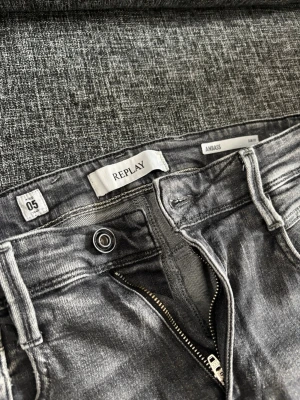 Gråa Replay Anbass jeans - Snygga gråa jeans från Replay, modell Anbass. Jeansen har klassisk femficksdesign, dragkedjegylf och detaljerade sömmar. Märkespatch bak i midjan och slim fit passform. Perfekta för en trendig och avslappnad stil.