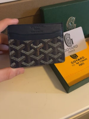 Mörkblå blå kortfodral plånbok  från Goy4ard - Snyggt svart kortfodral från Goy4ard med det klassiska mönstret i vitt och grått. Fodralet har flera kortfack och är tillverkat i canvas med läderdetaljer. Perfekt för dig som vill ha en stilren och exklusiv accessoar från ett ikoniskt märke.