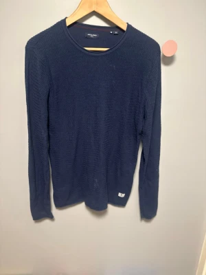 Jack & Jones - Säljer en mörkblå långärmad tröja från Jack & Jones. Tröjan har en diskret struktur i tyget och rund halsringning. Passar perfekt till jeans eller chinos för en enkel och stilren look.