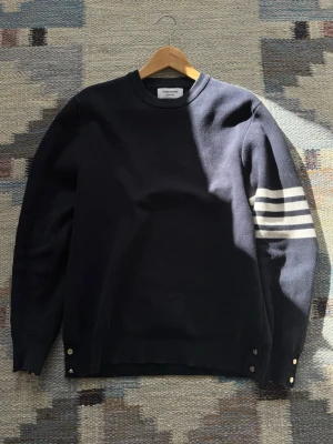 Mörkblå Thom Browne Tröja - THOM BROWNE Milano Stitch Crew Neck - Navy Storlek 3 (herr), men har krympt i tvatten och motsvarar nu ungefär en storlek 2. Tröjan är i bra skick, men lite nopprig. En extra knapp medföljer :)