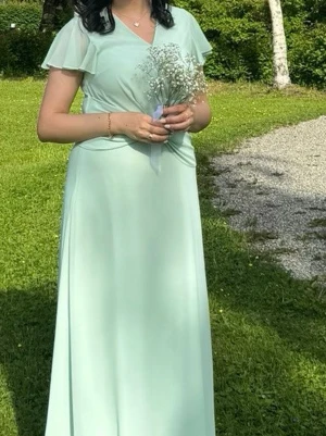 Ljusgrön långklänning med omlott - Säljer en elegant ljusgrön långklänning med omlottdetalj i midjan och v-ringad hals. Klänningen har korta, fladdriga ärmar och ett mjukt, fallande tyg som ger en romantisk känsla. Perfekt för sommarens speciella tillfällen.
