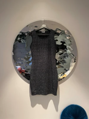 Glittrig svart kortklänning från only  - Snygg svart glittrig klänning från only med ärmlös design och rund halsringning. Klänningen har en kroppsnära passform och är perfekt för dig som vill sticka ut. Materialet är mjukt och stretchigt syntet med glittereffekt.