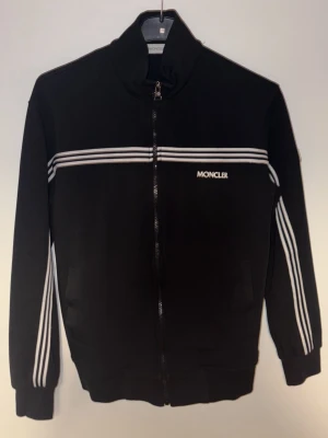 Tröja och byxa set från Moncler - Snygg svart set från Moncler. Tillverkad i mjukt material som passar perfekt till en sportig och avslappnad stil. Enbart testad fåtal tillfällen. Säljs som set. Kommer från ett rök/djurfritt hem