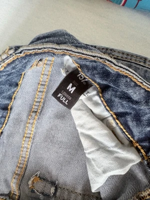 Blå jeans från 157 Paris Stitch M - Säljer ett par klassiska blå jeans från 157 Paris Stitch i storlek M. Jeansen har kontrastsömmar i gult och normal passform, jeansen är förkortade så passar för dom mellan 150-160 