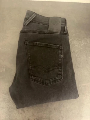 Svarta slim fit Replay Anbass stl 31 - Snygga svarta slim fit jeans från Replay med klassisk femficksdesign och diskret logga på bakfickan. Jeansen har normal midja och raka ben. Tillverkade i mjukt denimtyg som ger en skön passform och stilren look.