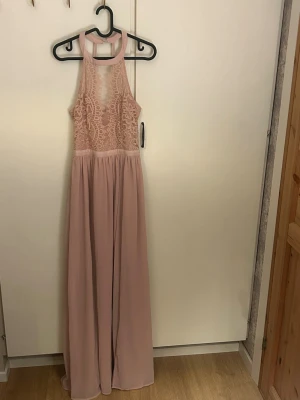 Lång rosa spetsklänning med halterneck - Långklänning i ljusrosa och spets från Nelly. Öppen i ryggen och en slit vid benet. Mycket bra skick endast använd en gång. Hör av vid frågor 