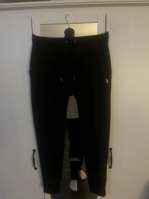 Svarta mjukisbyxor från Polo Ralph Lauren - Säljer ett par svarta mjukisbyxor från Polo Ralph Lauren med dragsko i midjan och ribbade benslut. Byxorna har en liten broderad logga på vänster sida och är tillverkade i mjukt material som passar perfekt för chill dagar. Hör av er vid frågor eller kom med prisförslag! Lite små noppriga.