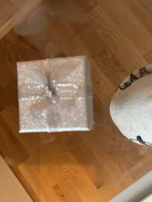 Silverfärgad smyckesask med rosett - En liten fyrkantig smyckesask i glittrande silver med dekorativ rosett på locket. Perfekt för att förvara eller ge bort smycken. Insidan är klädd i vitt tyg och har en liten bandögla för att hålla smycket på plats.