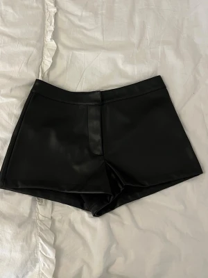 Svarta shorts i skinnimitation - Snygga svarta shorts i skinnimitation med midwaist passform. De har en stilren look utan synliga detaljer och är perfekta för dig som vill ha en edgy vibe. Passar till många olika stilar och är lätta att matcha med olika toppar.