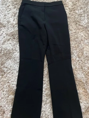 Svarta kostymbyxor med raka ben från HM - Snygga svarta kostymbyxor med raka ben och diskreta fickor både fram och bak. Byxorna har en klassisk midja och är perfekta för en clean och stilren look. Materialet är mjukt och lite stretchig vilket gör dem bekväma att bära hela dagen. Byxorna är från HM i storlek 36