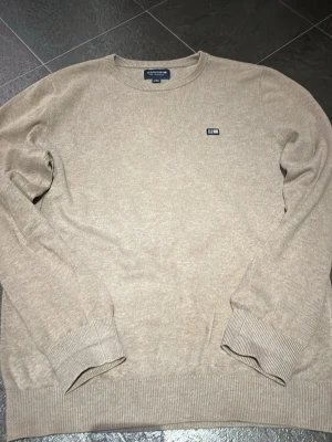 Beige tröja från Lexington - Klassisk beige tröja från Lexington med rund halsringning och diskret logga på bröstet. Tillverkad i mjukt material med ribbade muddar vid ärmar och nederkant. Perfekt för en stilren och enkel look. Passar XS. Ordinarie pris 900kr