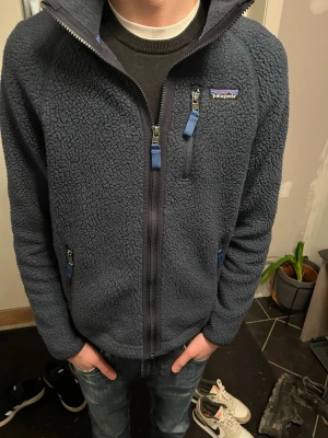 Blå fleecejacka från Patagonia - Rinktigt fet mörkblå fleecejacka från Patagonia med hel dragkedja, tre fickor med blå detaljer på dragkedjorna och hög krage. Perfekt för lager-på-lager och riktigt skön att ha på sig under kyliga dagar och perfekt ny till våren. Klassisk och stilren design. Ge prisförslag!!