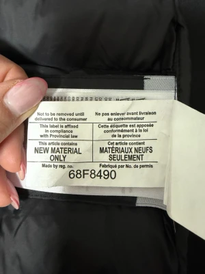 Svart väst från Canada Goose - Säljer en svart dunjacka från Canada Goose med klassisk rund logotyp på insidan. Jackan är vadderad med nytt material och har en stilren, quiltad design som håller dig varm under kalla vinterdagar. Materialet är slitstarkt och jackan har en tidlös look. Använd några gånger. 