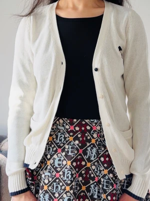 Uniform Teenie Weenie-kofta i krämvitt - Söt Teenie Weenie-kofta i krämvitt, stl M (165/88A) Charmig och mjuk kofta i preppy stil med broderad björnlogga. V-ringning och knäppning fram, passar perfekt till vardag eller skola. I mycket gott skick. Material: 82,6 % bomull, 17,4 % akryl. Mått: axel 36 cm, ärm 64 cm, längd 62 cm. Hämtas i Kista eller skickas.