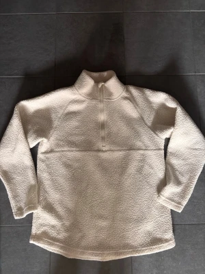 Vit teddytröja  - Mysig vit teddytröja med halv dragkedja framtill och hög krage. Tröjan har lång ärm och är gjord i fluffigt, mjukt material som håller dig varm. Perfekt för kalla dagar och enkel att matcha med jeans eller leggings. Pile fleece 