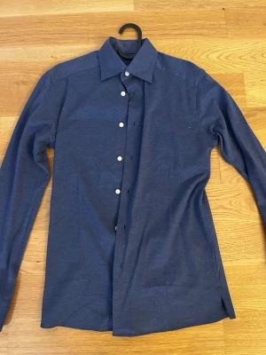 Mörkblå skjorta - Snygg mörkblå skjorta med klassisk krage och vita knappar. Skjortan har lång ärm och rak passform, perfekt för en stilren look. Materialet känns mjukt och bekvämt mot huden.