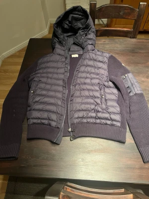 Mörkblå pufferjacka från Moncler - Snygg mörkblå pufferjacka från Moncler med stickade ärmar och huva. Storlek L men är som M. Moncler-logga på ärmen. Perfekt för kalla dagar och riktigt trendig look. Hör av dig vid frågor