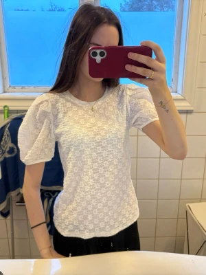 Vit topp med puffärmar från H&M - Säljer en söt vit topp från Vero Moda med puffärmar och diskret struktur i tyget. Toppen har rund halsringning och är tillverkad i ett lätt och luftigt material som passar perfekt till jeans eller kjol.