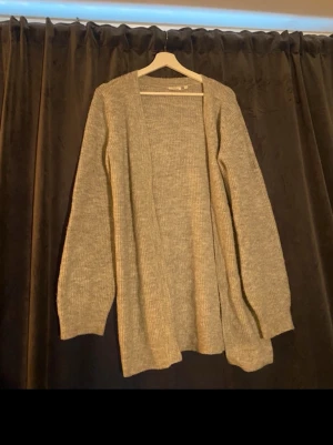 Ljusgrå stickad kofta Gina Tricot - Mysig ljusgrå stickad kofta från lager 157 med öppen front och långa ärmar. Koftan har en avslappnad passform och ribbstickad struktur, perfekt att slänga över en t-shirt eller topp för en chill look.