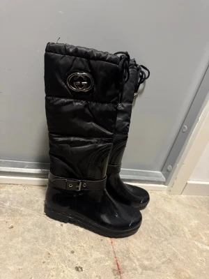 Svarta nya stövlar  - Säljer ett par svarta stövlar med blank yttersida, quiltad textil upptill och fuskpälsfoder. Stövlarna har snörning upptill och dragkedja. Perfekta för kalla dagar och riktigt snygga till jeans eller leggings. Använda 1 ggn! 