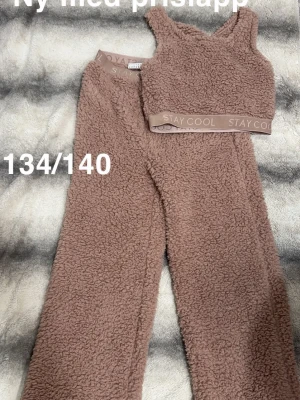 Rosa teddy-loungewear set  - Mysigt loungewear set i rosa teddyfleece från Lindex. Setet består av ett linne med breda axelband och resår under bysten samt matchande vida byxor med resår i midjan. Perfekt för chill dagar hemma och supermjukt material.🌸 Ny med lapp. Storlek 134/140 