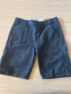 Mörkblå shorts från Lindex - Snygga mörkblå shorts från Lindex i regular fit. Klassisk design med bälteshällor, fickor fram och dragkedja. Perfekta för sommaren och enkla att matcha med olika stilar.