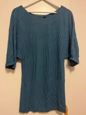 Blå ribbstickad tröja från H&M - Säljer en blå ribbstickad tröja från H&M med halvlånga ärmar och bred rund halsringning. Tröjan har en smickrande passform och är tillverkad i ett mjukt, stretchigt material som känns skönt mot huden.