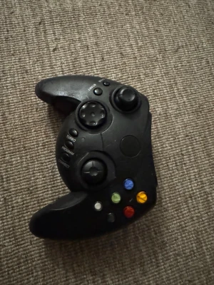 Xbox original handkontroll svart - Klassisk svart handkontroll till Xbox original med färgade knappar och ergonomisk form. Perfekt för dig som vill spela retrospel eller samla på gamla konsoler. Tillverkad i plast med tydliga knappar och rejäla grepp. OBS Handkontrollen fungerar bra, men den är lite klibbig och behöver bara rengöras